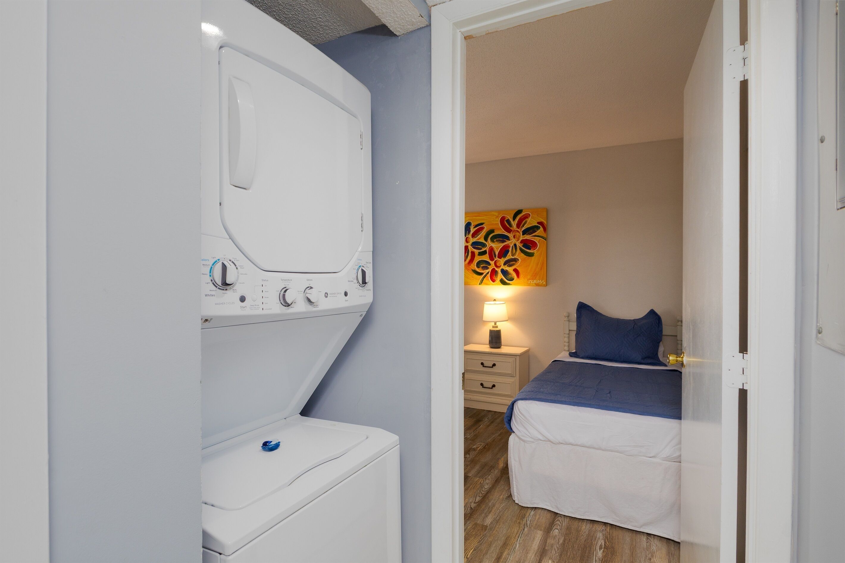 Quarto com cama, mesa de cabeceira, luminária e máquina de lavar.