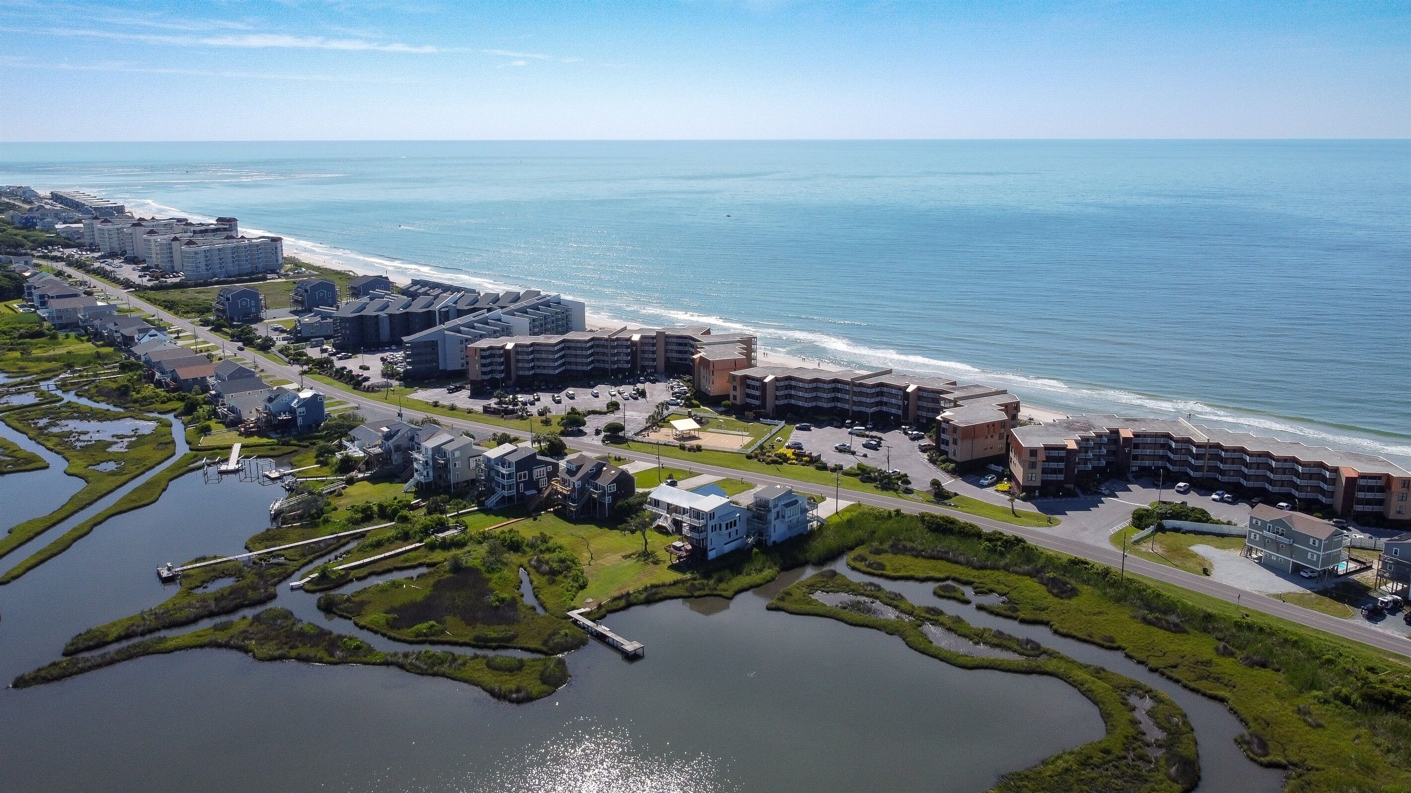 An aerial view of a coastal hotel area with multiple buildings, a beach, and a marina.