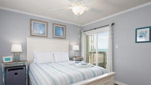 A bedroom with a bed, two bedside tables, a ceiling fan, and a window with a view. - Oceanfront Comfort at "Coastal Wonderland" (North Topsail Beach)