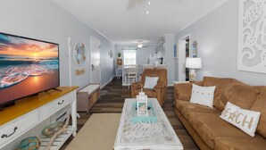 A living room with a TV, a brown couch, a coffee table, and a dining area in the background. - Oceanfront Comfort at "Coastal Wonderland" (North Topsail Beach)
