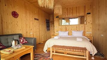 Interior de una cabaña de madera con cama, sofá, mesa y lámpara colgante.