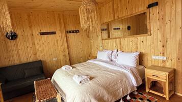 Una habitación con paneles de madera, una cama, un sofá, una mesita de noche de madera y una lámpara colgante tejida.