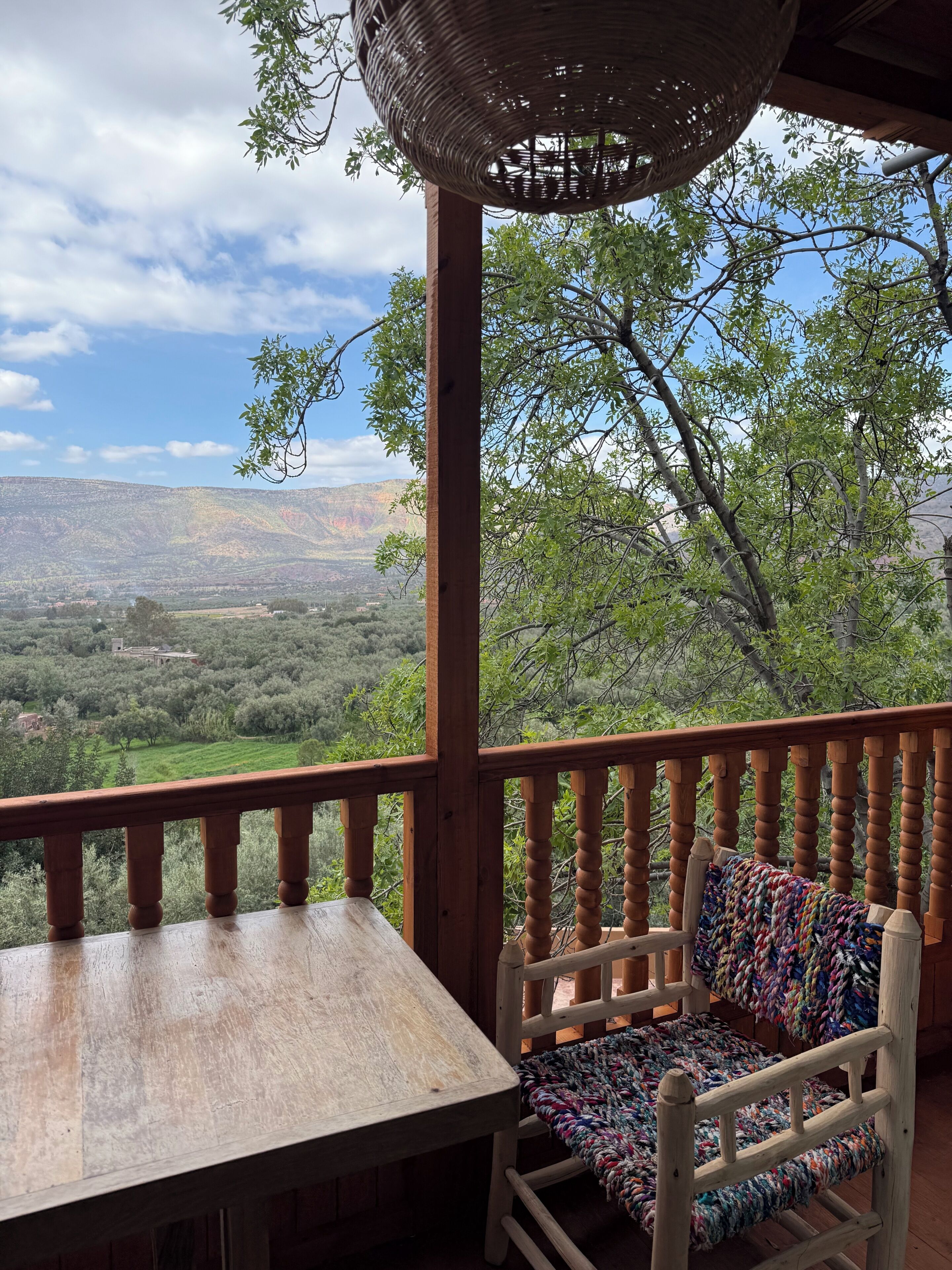 Une terrasse en bois avec une table et une chaise en osier, offrant une vue sur un paysage montagneux.