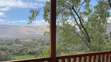 Une terrasse en bois avec une table et une chaise en osier, offrant une vue sur un paysage montagneux.