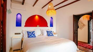 Un dormitorio con cama, mesita de noche, pared de acento roja y lámpara colgante.