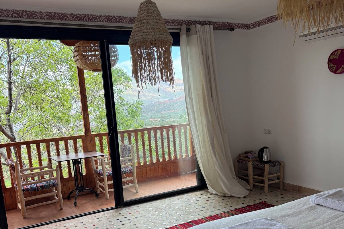 Une chambre avec un lit, une vue sur l’extérieur, un balcon avec des chaises et un sol à motifs.