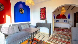 Une pièce comprenant un canapé, une petite table, un lit doté d’un baldaquin rouge et un tapis à motifs.