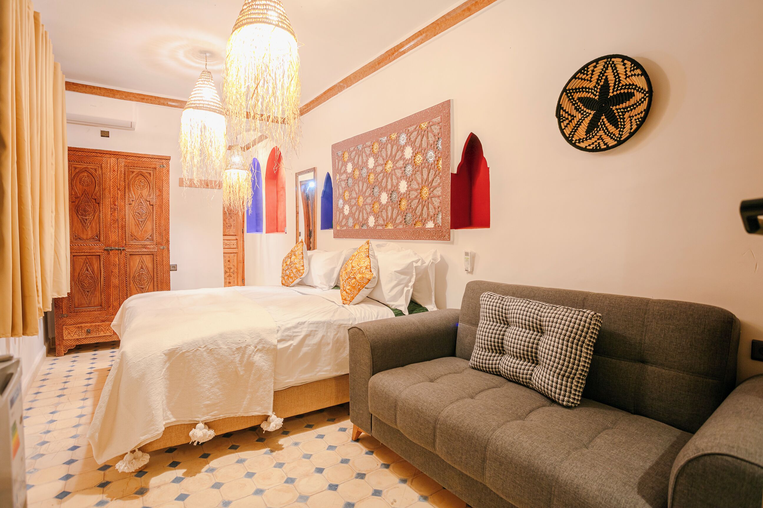 Une chambre à coucher comprenant un lit, un canapé, un lustre, une armoire en bois et une décoration murale à motifs.