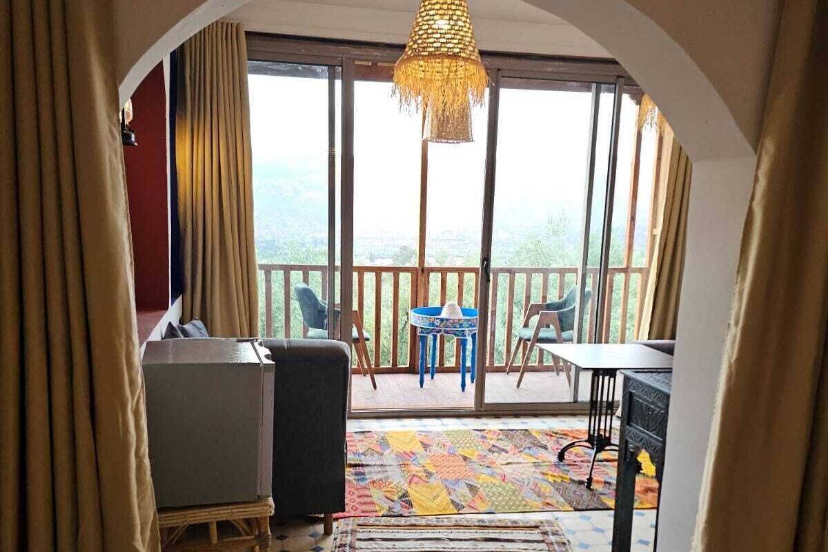 Une pièce chaleureuse avec une grande fenêtre, un tapis à motifs et une vue sur l’extérieur.