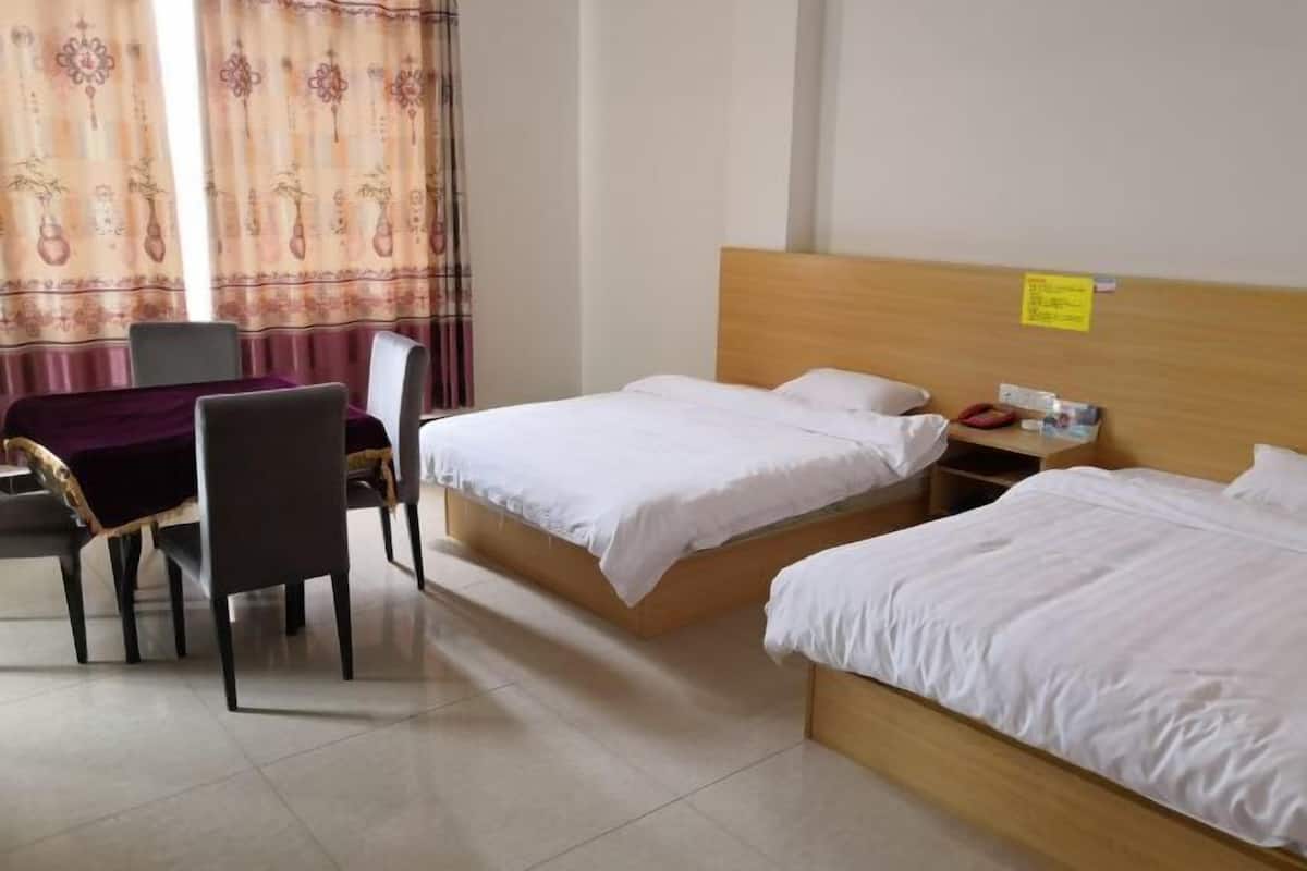 A hotel room with two beds, a wooden headboard, a small table with chairs, and a curtain with a floral pattern.