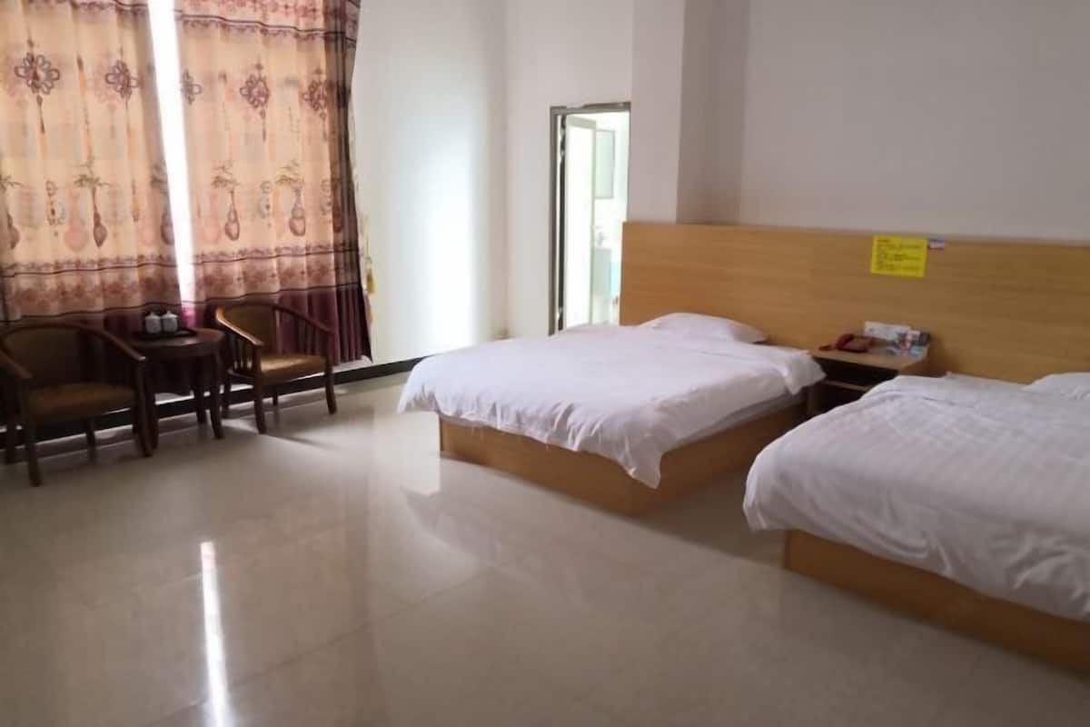 A hotel room with two beds, a wooden headboard, a small table with a chair, and a window with curtains.