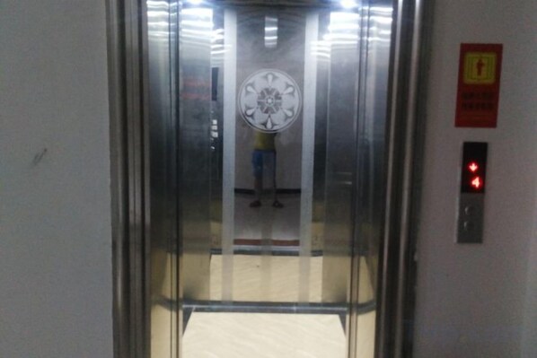 An elevator with a glass door, a red emergency exit sign, and a control panel with a red light.