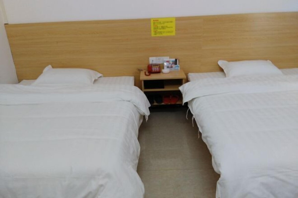 A room with two single beds, a wooden headboard, a nightstand with a red object, and a yellow sign.