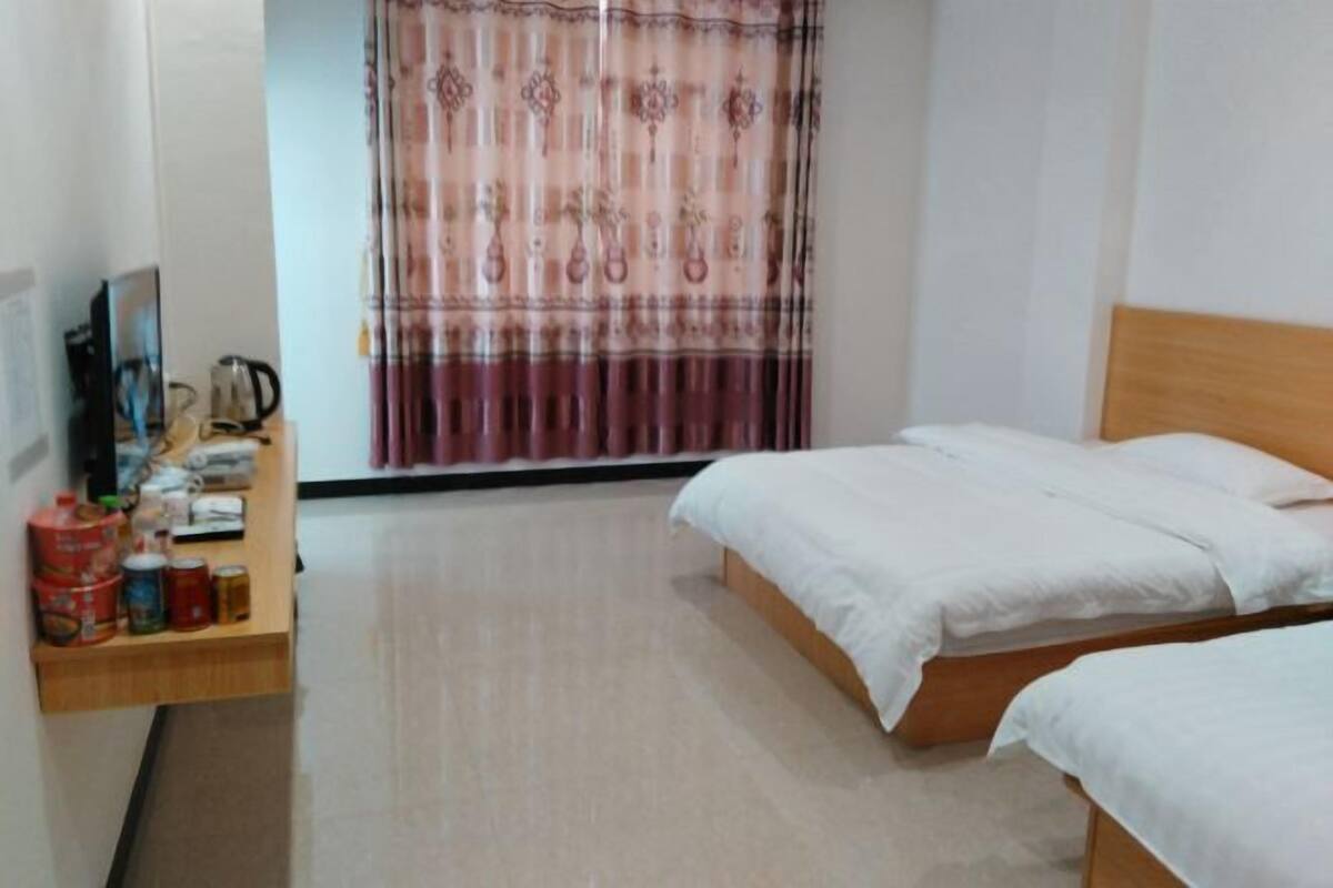 A hotel room with two beds, a wooden nightstand with various items, and a curtain with a floral pattern.