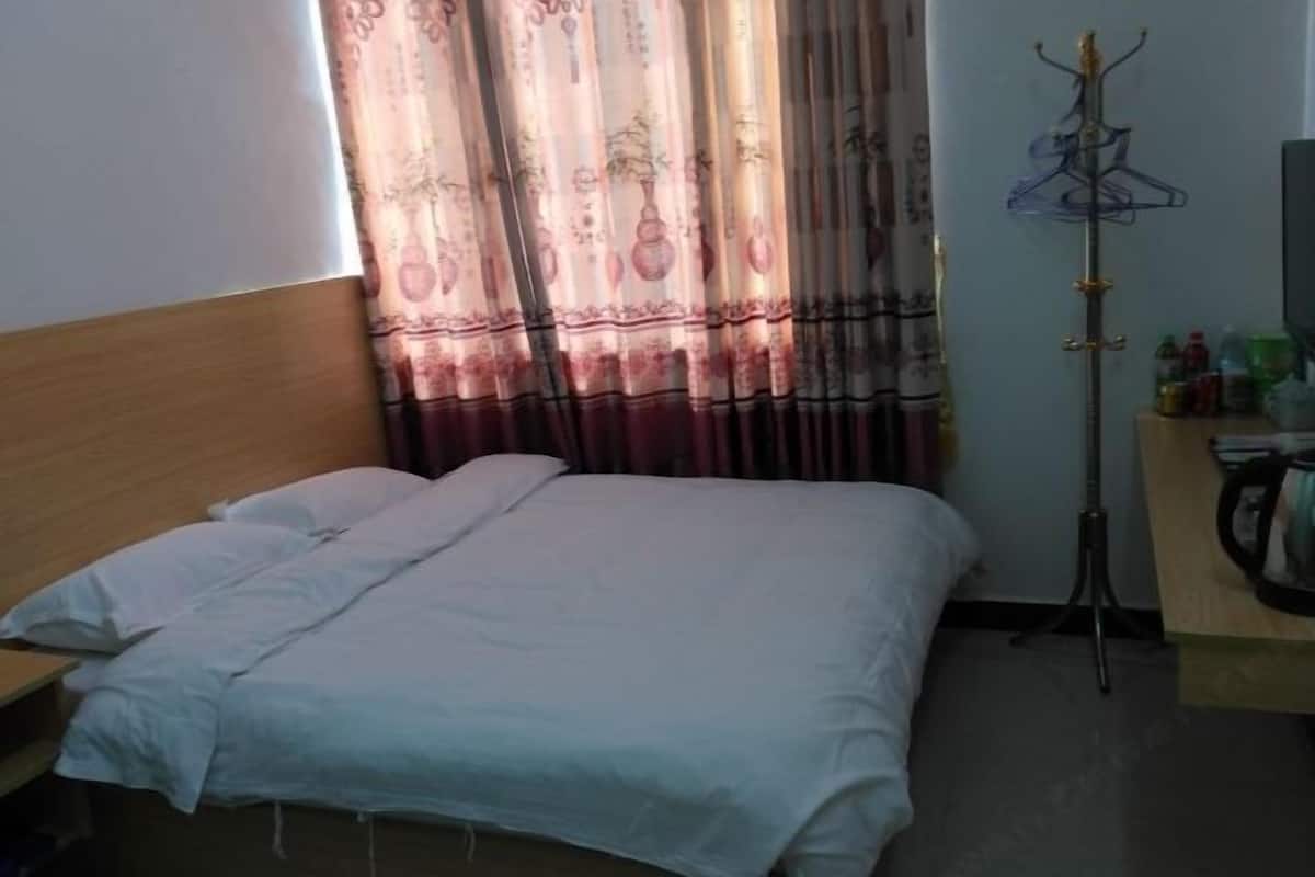 A single bed with white bedding, a wooden headboard, a coat rack with hangers, and a small table with toiletries.