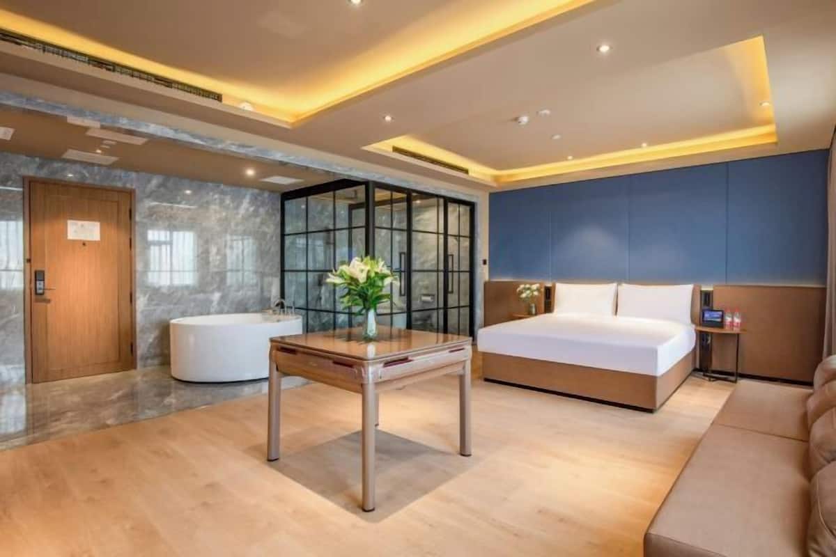 A modern hotel room with a large bed, a wooden table, a glass partition, and a marble wall.