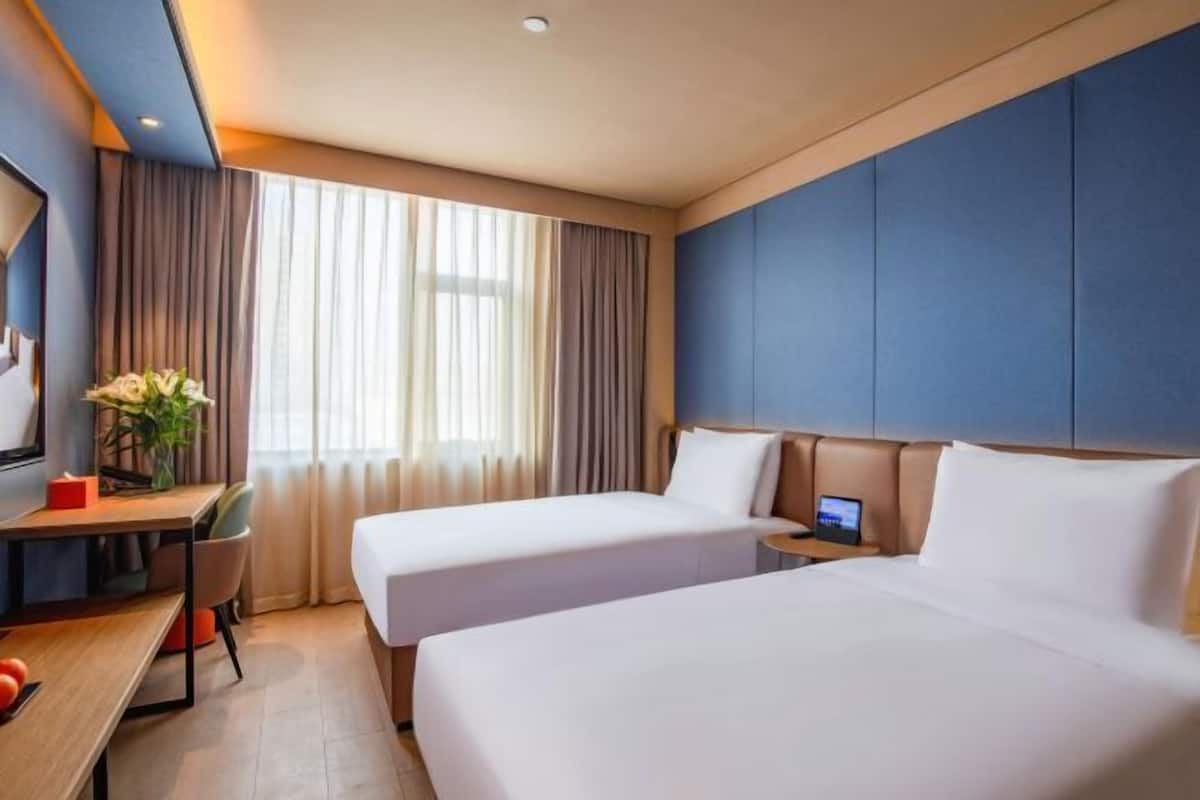 A hotel room with two beds, a desk, a chair, a TV, and a window with curtains.