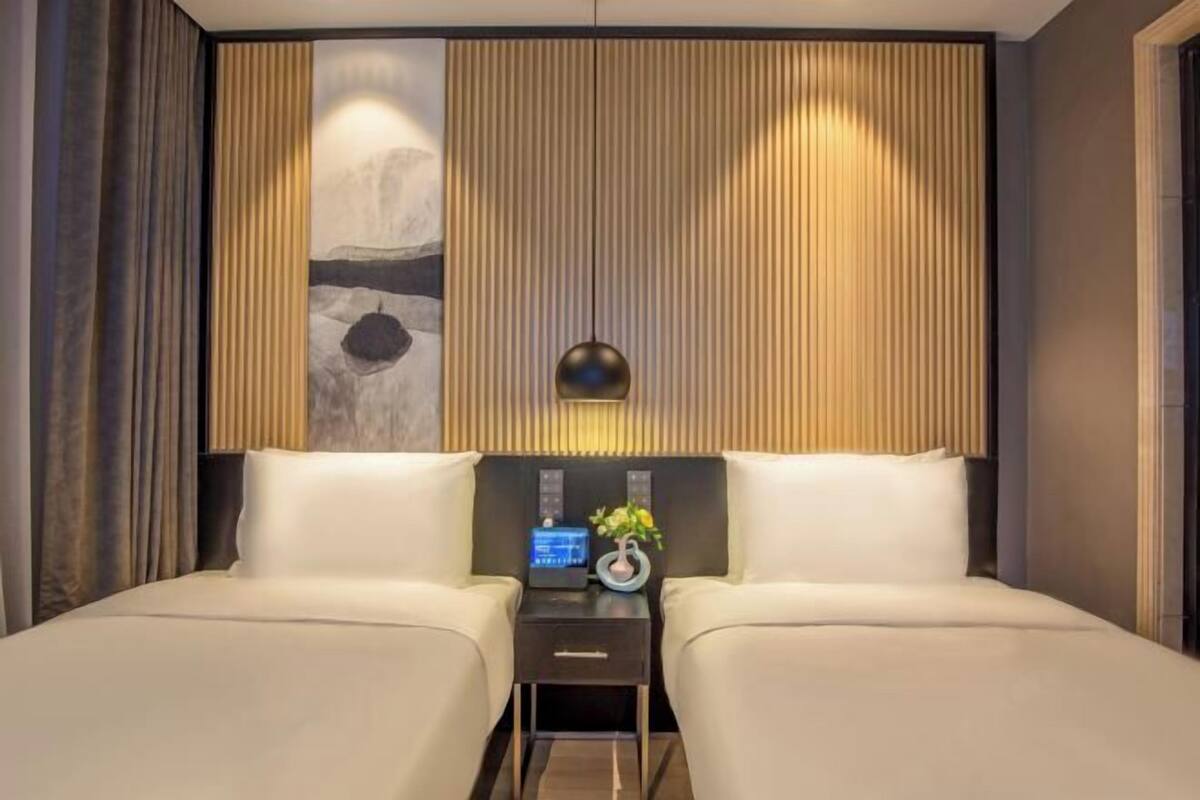 A modern hotel room with a large bed, a bedside table with a radio, and a decorative wall panel.