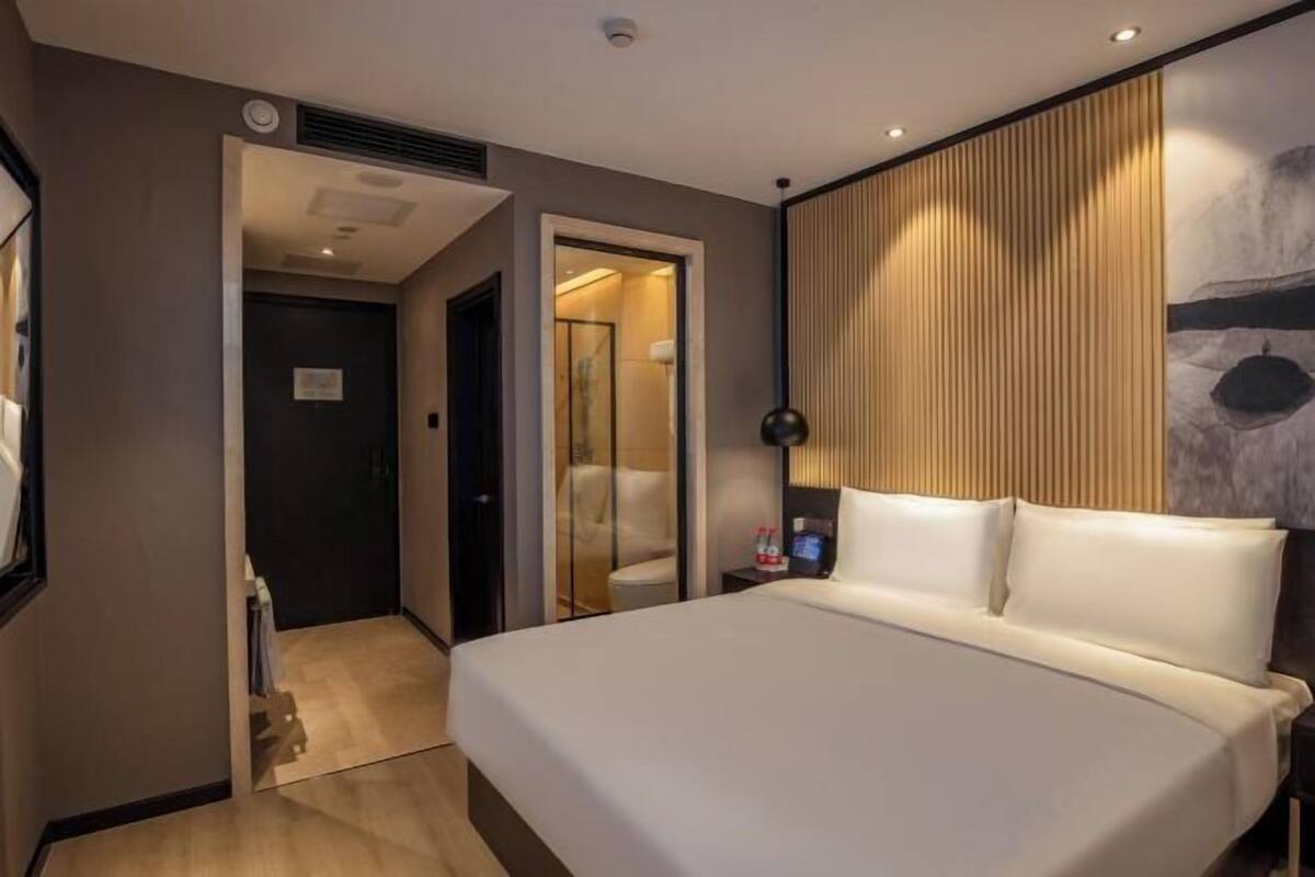 A hotel room with a large bed, a bedside table with a lamp, and a view of a mountainous landscape through a window.