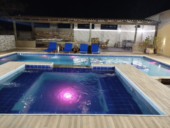 A swimming pool with blue tiles, a wooden deck, and a waterfall feature.