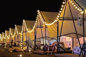 Række af telte med lyskæder, hver med et lille bord og stole, og et skilt med kinesiske tegn.