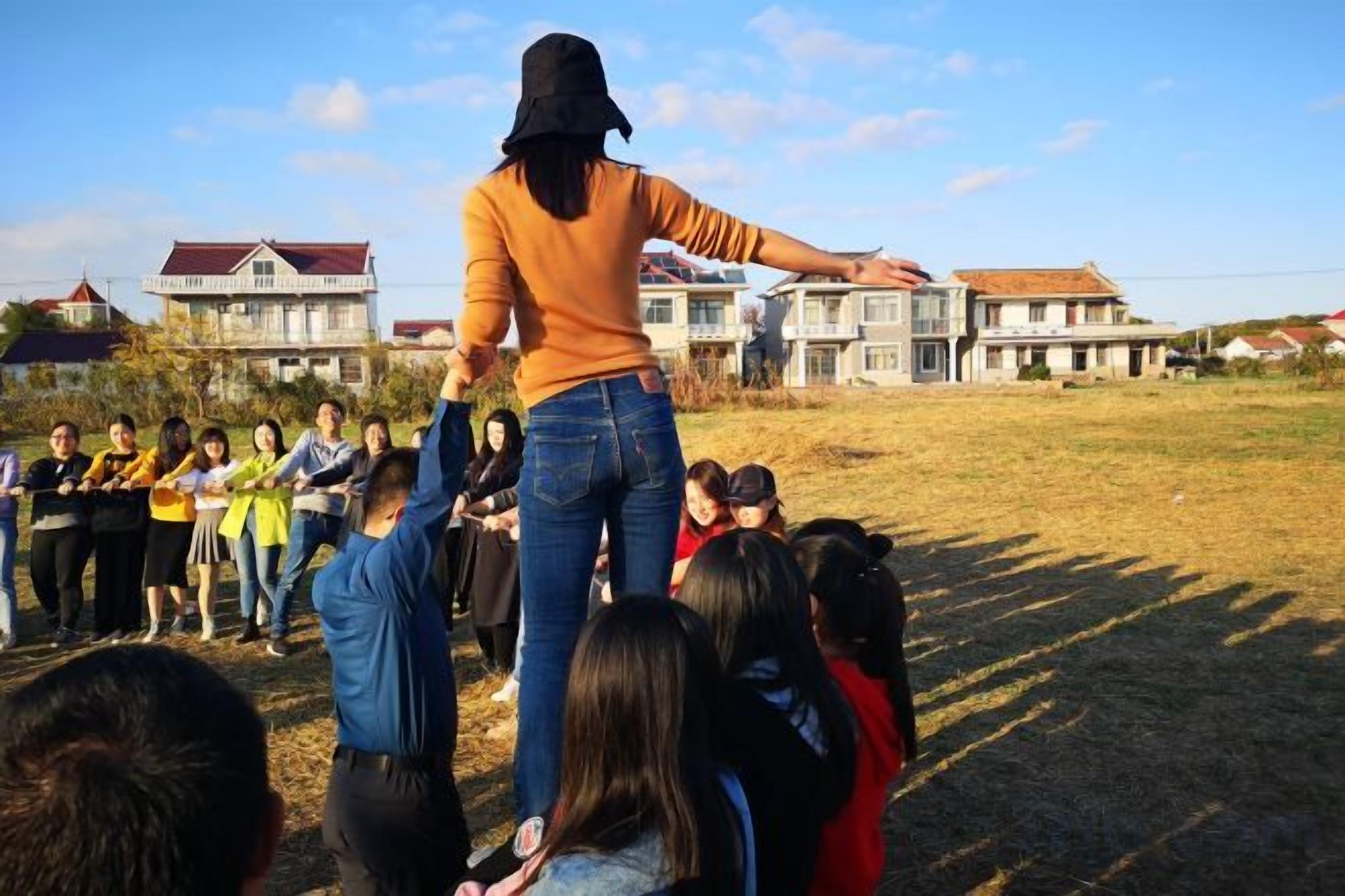 Una persona alçada en un camp de gespa amb un grup de persones a sota, davant d'edificis residencials.