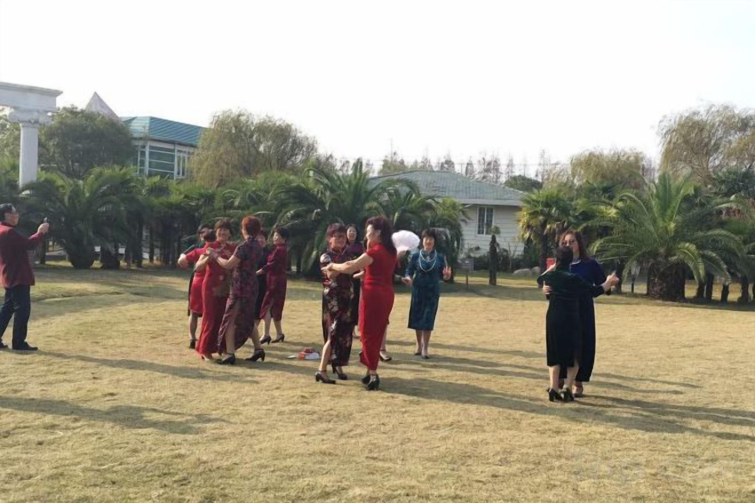 A group of people in a grassy outdoor area with trees and a building in the background.