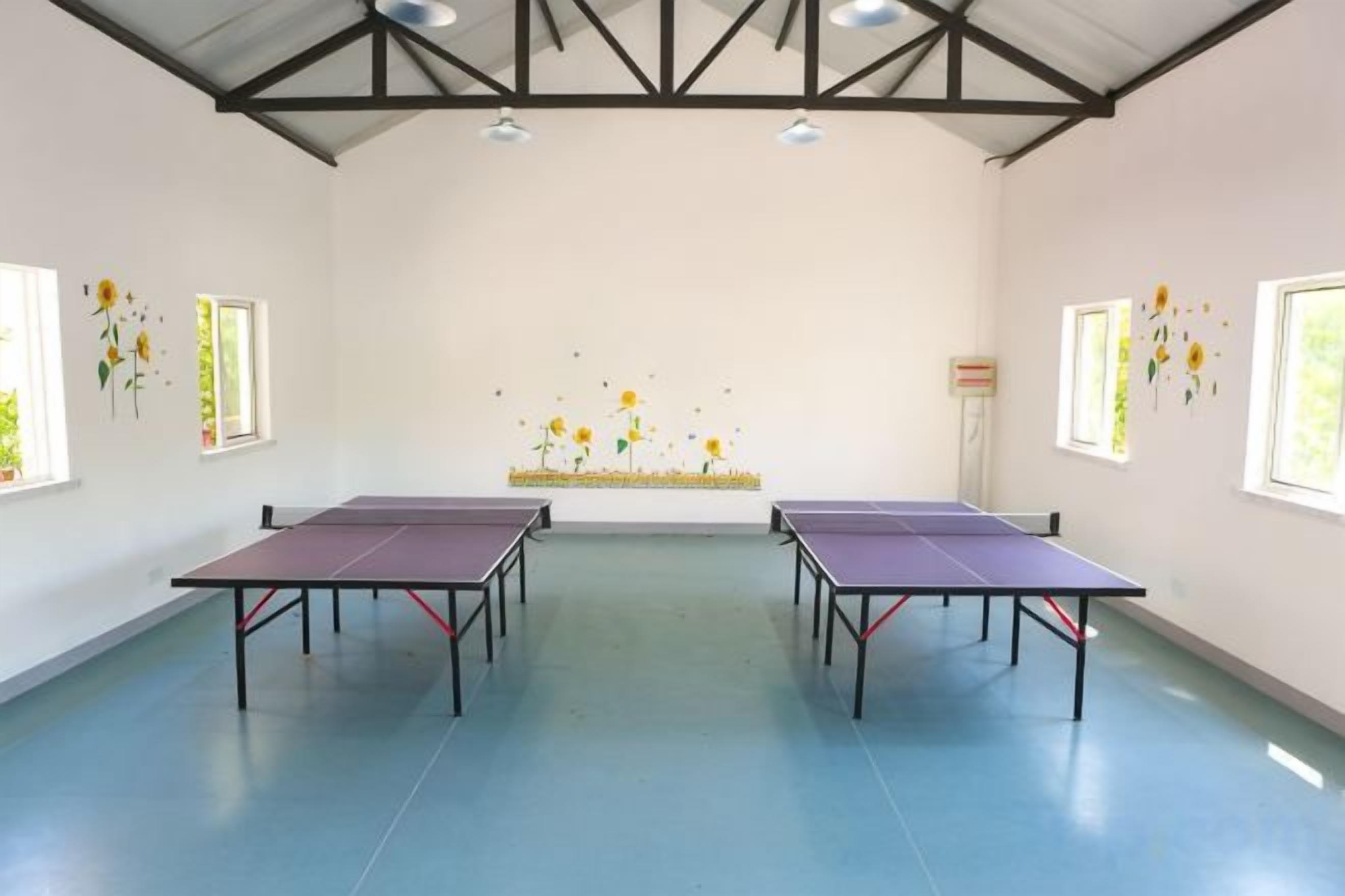 A room with four ping pong tables, a high ceiling with trusses, and windows with flower decals.