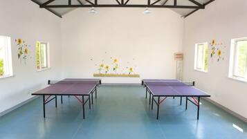 A room with four ping pong tables, a high ceiling with trusses, and windows with flower decals.