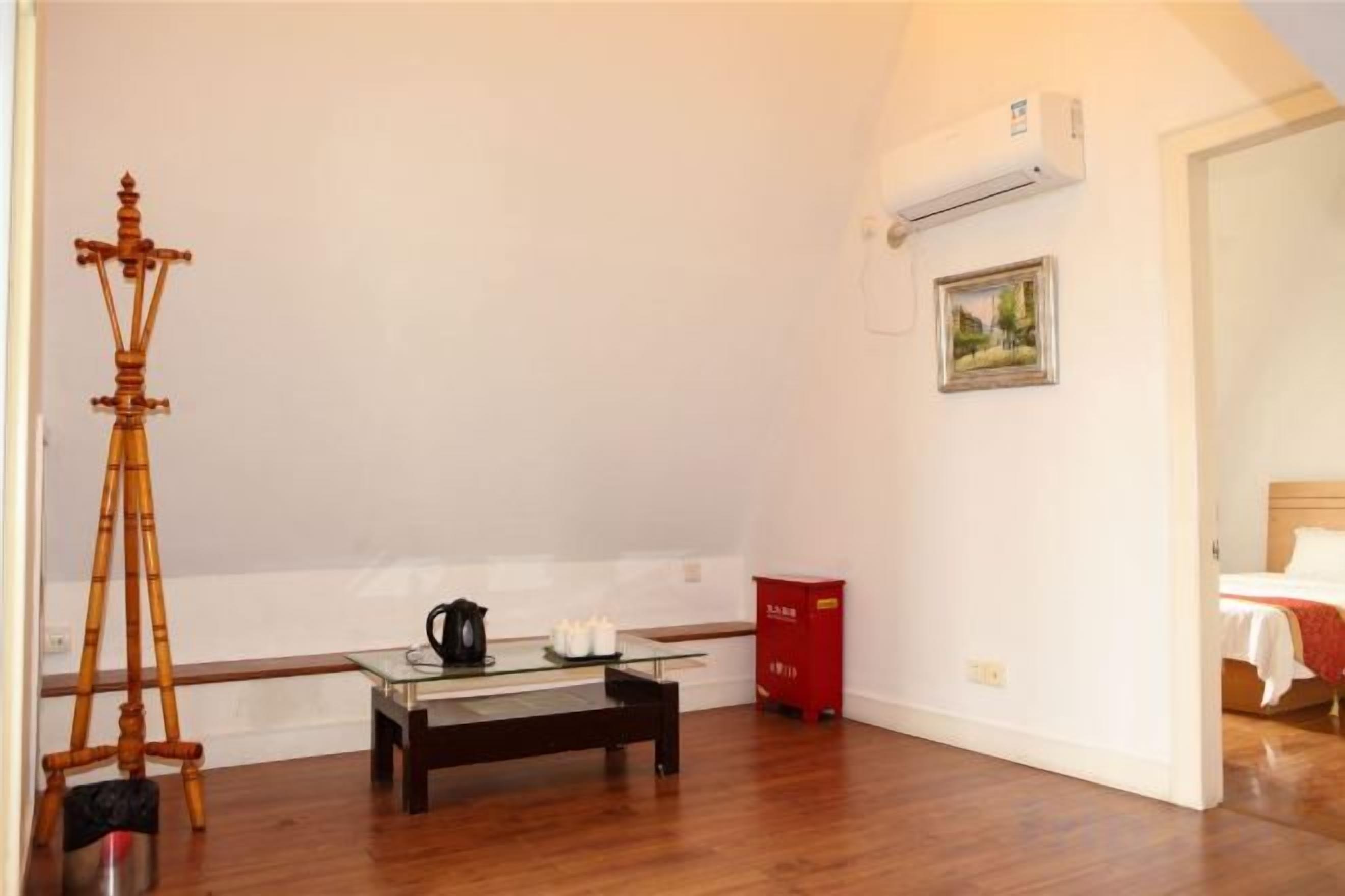 A room with a wooden floor, a glass-top table with a kettle and teapot, a tripod, a red trash bin, and a framed picture on the wall.