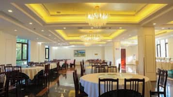 A spacious dining area with multiple tables and chairs, a chandelier, and a view of the outdoors.