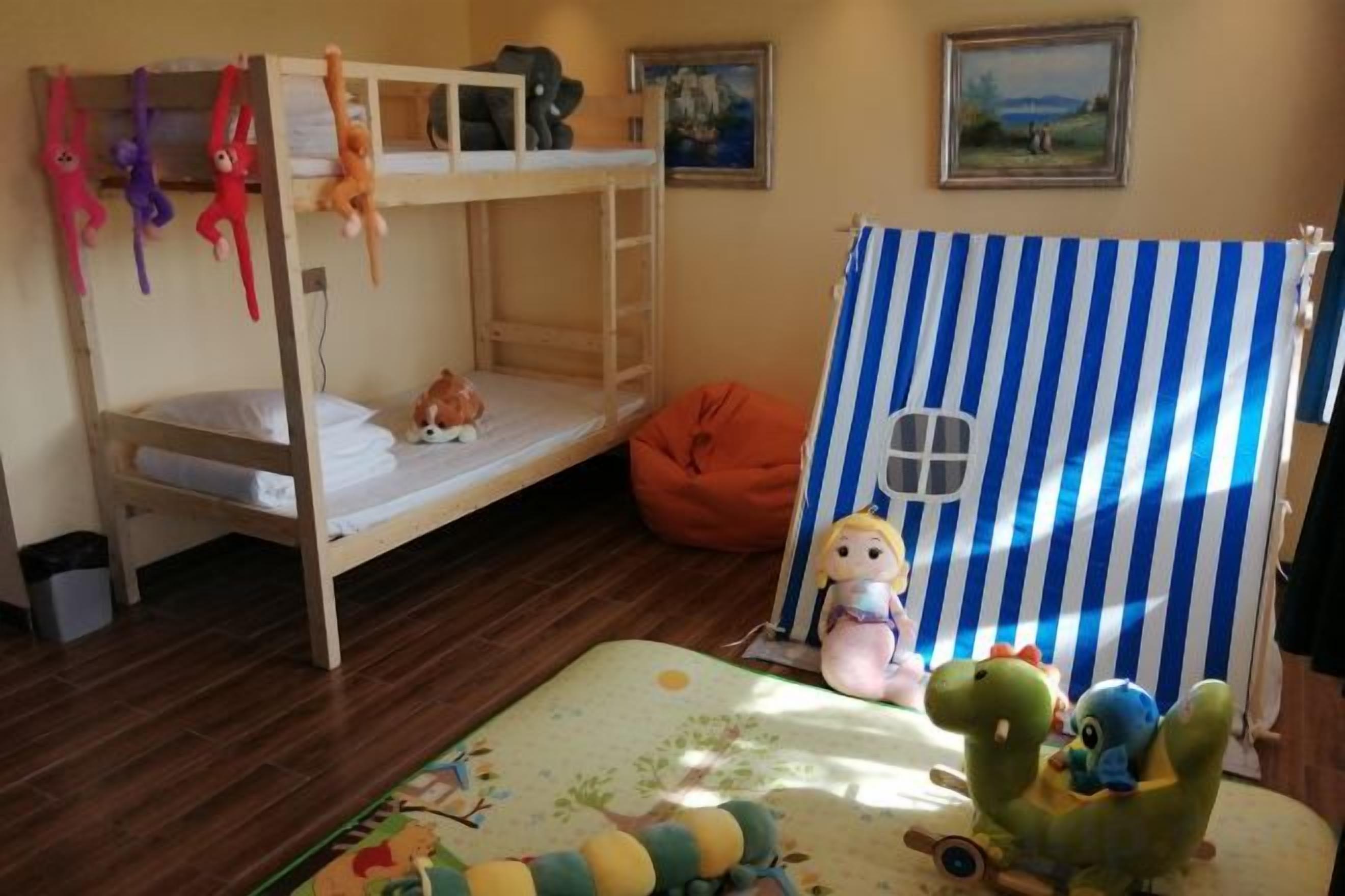Una cama litera con juguetes, un sillón de saco y una cortina a rayas.