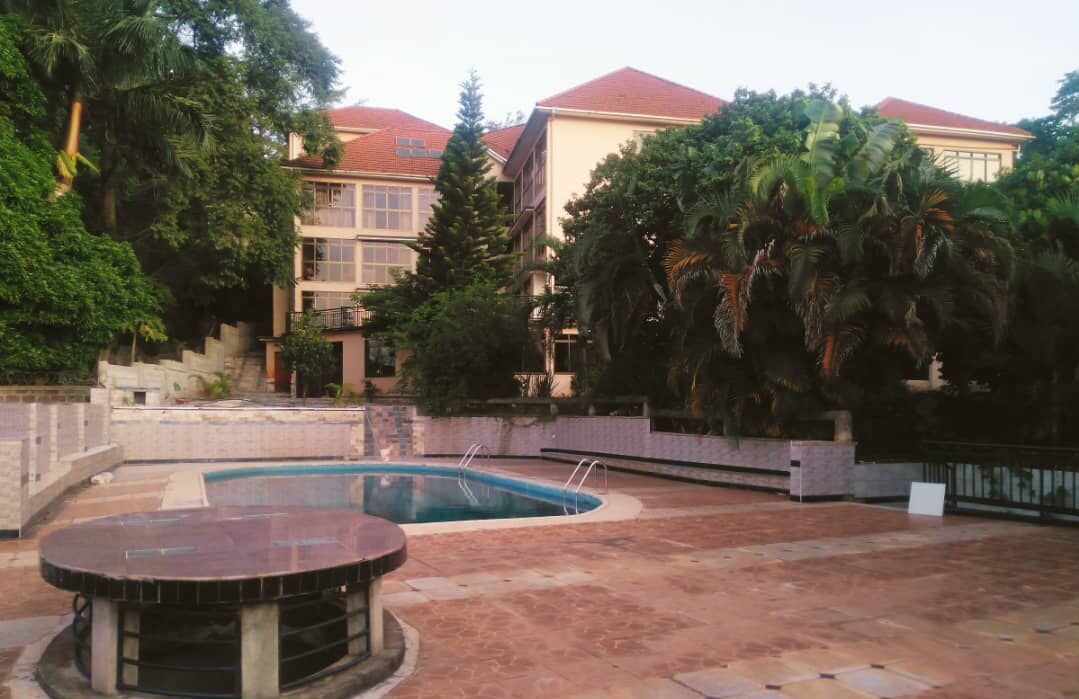 A swimming pool surrounded by a patio area with a stone floor, a round table, and a building with a red roof in the background.