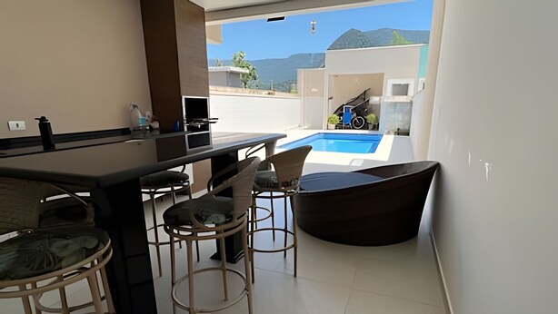 A modern kitchen with a bar area, a pool, and a view of the mountains. - Casa com piscina em Boraceia (Bertioga)