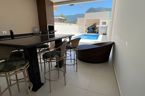A modern kitchen with a bar area, a pool, and a view of the mountains. - Casa com piscina em Boraceia (Bertioga)