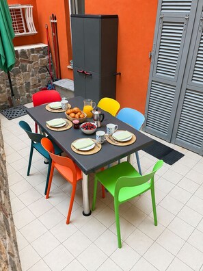 A dining area with a table set for two, surrounded by colorful chairs, a stone wall, and a metal cabinet.