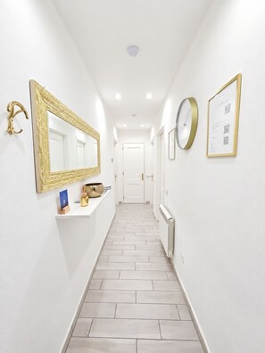 A hallway with a white floor, a wall-mounted mirror, a clock, and a framed document. - Best Stay Apartment (La Spezia)