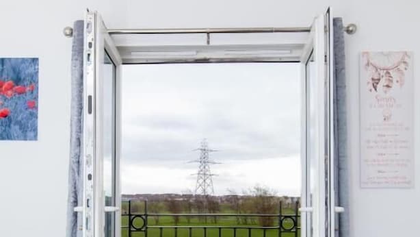 A bedroom with a bed, a view of a green field, and a metal gate.