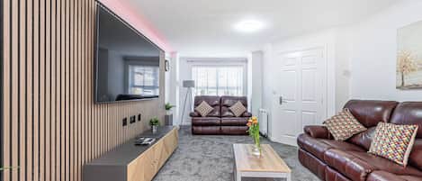 A modern living room with a sofa, a coffee table, and a TV mounted on a wooden wall.