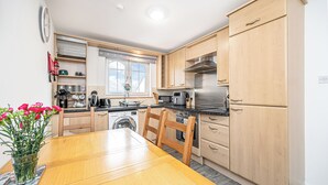 A modern kitchen with wooden cabinets, a stainless steel range hood, and a dining area with a wooden table and chairs. - Super Prime Train Station Inverkeithing by Three Bridges Apartments (Inverkeithing)