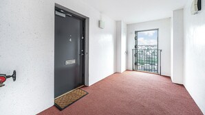 A hallway with a door marked '4', a red carpet, a window with a view of a cityscape, and a balcony with a metal railing. - Super Prime Train Station Inverkeithing by Three Bridges Apartments (Inverkeithing)