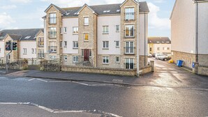 A multi-story residential building with a stone facade, multiple balconies, and a gated entrance. - Super Prime Train Station Inverkeithing by Three Bridges Apartments (Inverkeithing)