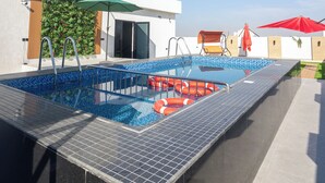 Ein Pool auf dem Dach, mit blauem Himmel, einer grünen Wand mit Pflanzen und einem roten Sonnenschirm.