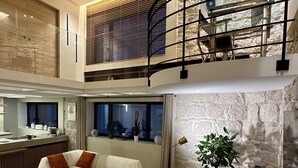 Un interior moderno con sofá, mesa de centro y zona de comedor con techo alto y pared de piedra vista.