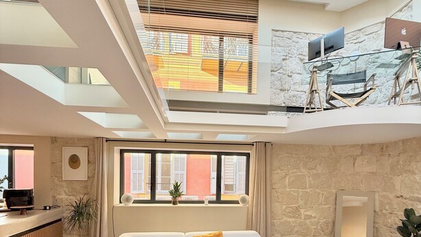 Un amplio salón con techo alto, un sofá modular, una mesa de centro y vistas al exterior a través de grandes ventanales.