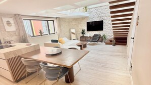 Una sala de estar moderna con una mesa de comedor de madera, un sofá y un televisor montado en una pared de piedra.
