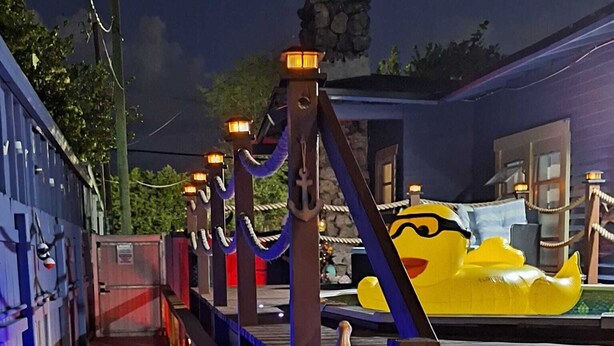 A wooden deck with a railing, a yellow inflatable boat, and a statue of a character. - Blue Little Havana (Miami)