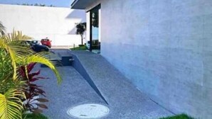 A modern building with a flat roof, a paved pathway, and a small garden area with palm trees.