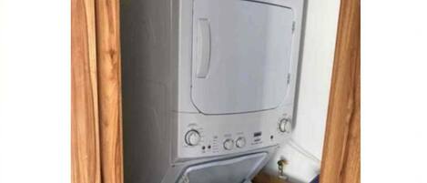 A compact, white washing machine with a front-loading door, installed in a corner with wooden framing.
