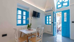 A dining area with a table and chairs, a TV mounted on the wall, and blue-framed windows. - Cycladic Traditional House with view by MPS (Emporio)